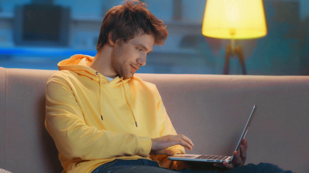 freelance concentrato utilizzando computer portatile e sorridente sul divano in soggiorno
 - Filmati, video