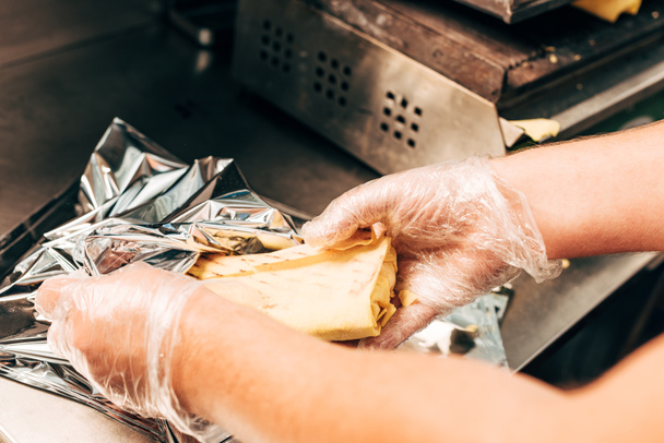 vista parcial de cocinero en guantes usando papel de aluminio mientras se prepara doner kebab
 - Foto, Imagen