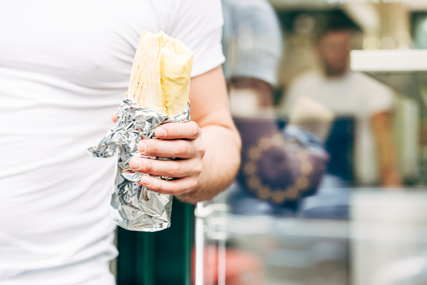 partial view of man holding doner kebab in aluminium foil - Φωτογραφία, εικόνα