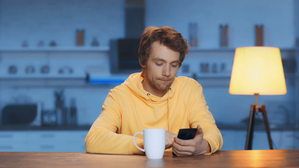 zaměřený mladý muž popíjení čaje a používání smartphone - Záběry, video
