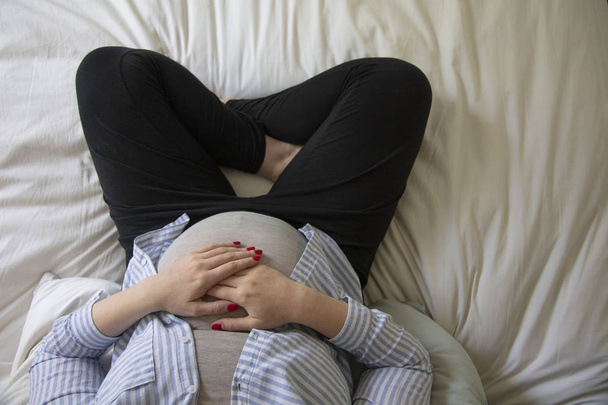Egy fiatal terhes nő pihen otthon ül egy ágyban. Várandós anya - Fotó, kép