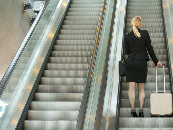 Empresaria parada en escalera mecánica con bolsas de viaje
 - Foto, Imagen