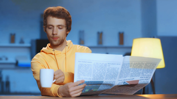 man drinking tea and reading newspaper at home at night - Materiaali, video