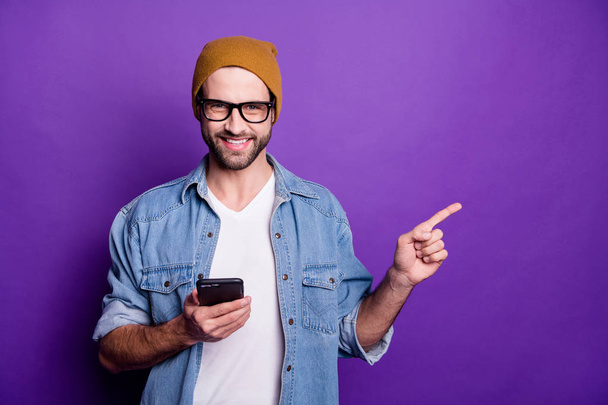 Photo of cool guy holding telephone indicating finger empty space wear jeans outfit isolated violet background - Foto, imagen