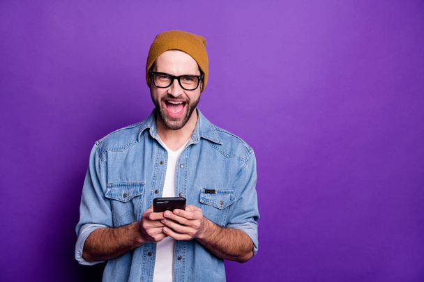 Cool handsome guy holding telephone reading unbelievable good news casual denim outfit isolated violet background - Foto, imagen