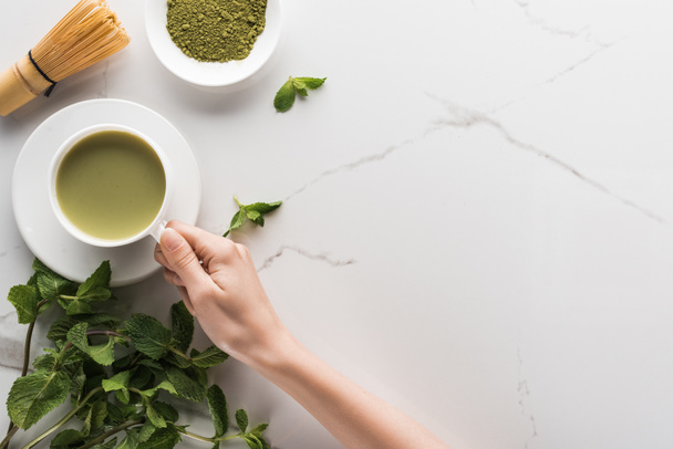 top view of woman holding matcha matcha tea on table with whisk, powder and mint  - Fotoğraf, Görsel