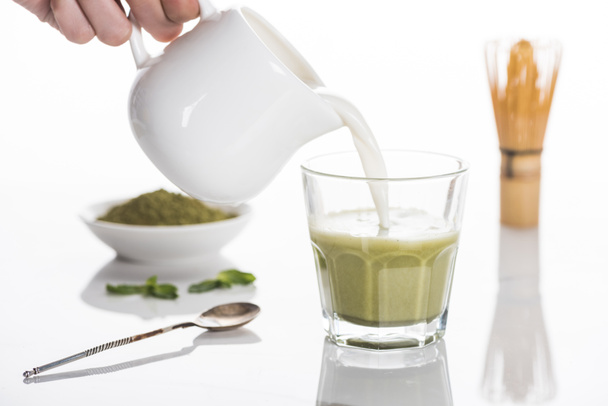 cropped view of woman pouring milk into matcha matcha tea on table with whisk and powder  - Φωτογραφία, εικόνα