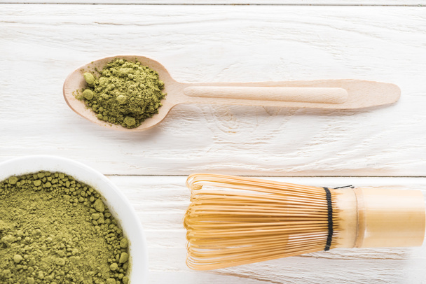 top view of wooden spoon with powder of green matcha tea and whisk - Foto, Imagem