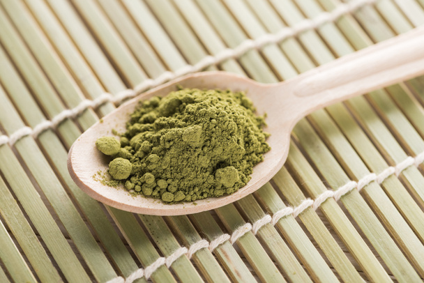wooden spoon with powder of green matcha tea on bamboo mat - Foto, Imagen