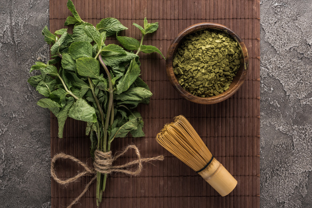 felülnézet zöld Matcha tea por, menta és habverővel a bambusz szőnyeg a sötét kő asztal - Fotó, kép