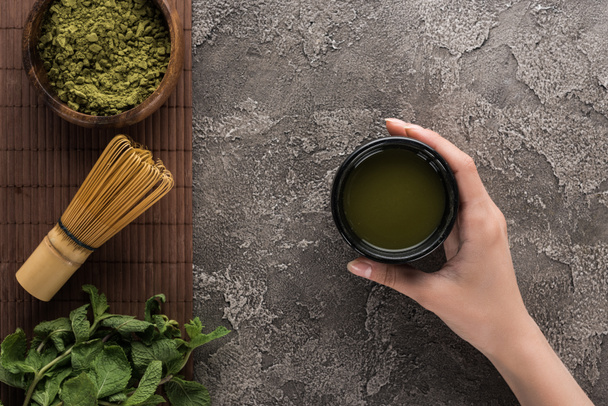 top view of woman holding matcha matcha tea on table with whisk, powder and mint  - Foto, Imagem