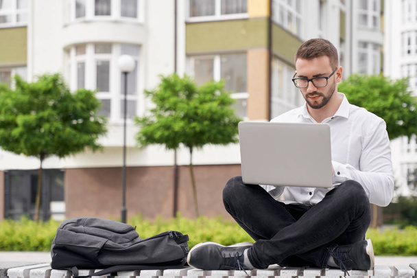 Man in glasses on bench holding laptop on knees, working. - Valokuva, kuva