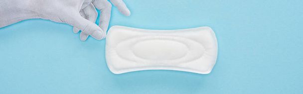 vista superior do papel branco mão segurando toalha sanitária de algodão no fundo azul, tiro panorâmico
 - Foto, Imagem