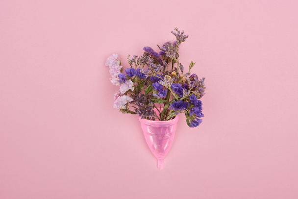 Κορυφαία όψη του ροζ πλαστικού εμμηνορροϊκό Κύπελλο με αγριολούλουδα απομονωμένα σε ροζ - Φωτογραφία, εικόνα