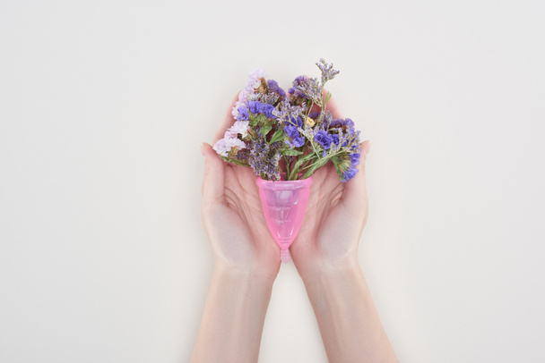 cropped view of woman holding menstrual cup with wildflowers isolated on grey - Zdjęcie, obraz