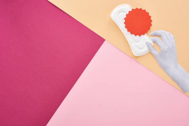 top view of white hand with sanitary towel and red card on pink, purple and beige background - Photo, Image
