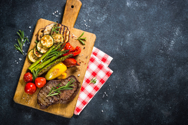 Rundvlees steak gegrild met groenten op zwarte stenen tafel. - Foto, afbeelding