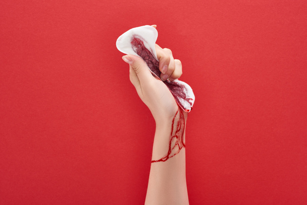 gedeeltelijke weergave van de vrouw knijpen sanitaire handdoek met bloed op rode achtergrond - Foto, afbeelding