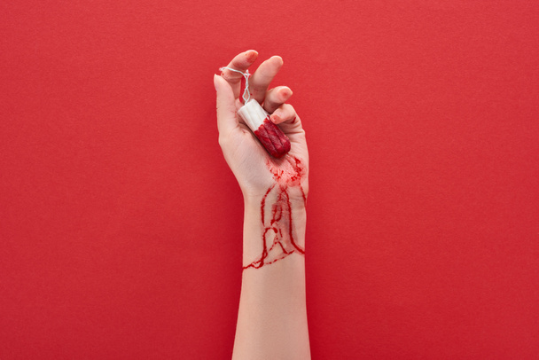 partial view of woman holding tampon with blood on red background - Photo, Image