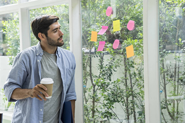 Handsome men, drinking coffee, business owners, use post it notes to thaink have idea. . Sticky note on glass wall. - Photo, Image