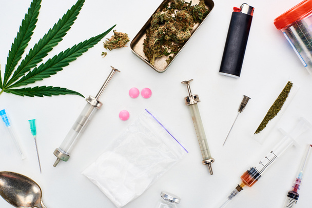 вид сверху на бутоны марихуаны, листья конопли, героин, ЛСД и шприцы на белом фоне
 - Фото, изображение