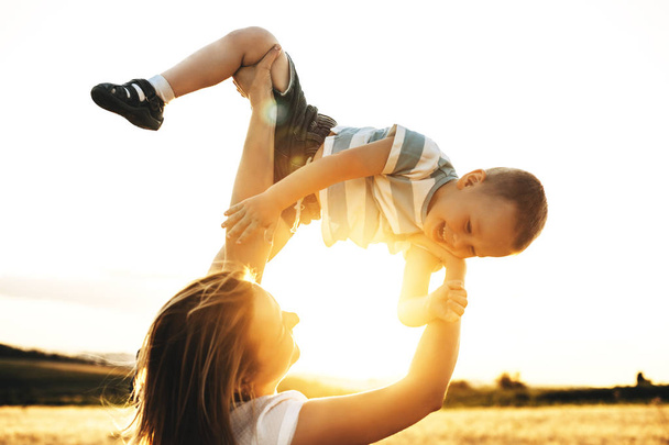 Genç beyaz anne gün batımı gülmek karşı oğlu ile oynuyor - Fotoğraf, Görsel