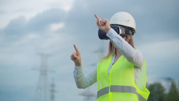 Portret nowoczesnej kobiety z mechaniki inżyniera przeprowadzając inspekcję poprzez okulary wirtualnej rzeczywistości i biały hełm, ubrany w mundur w tle wieże władzy - Materiał filmowy, wideo
