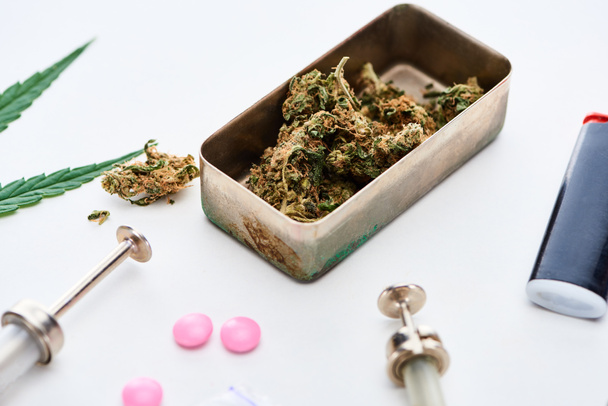 close up view of marijuana buds, syringes and lighter near pink ecstasy on white background - Foto, Imagem