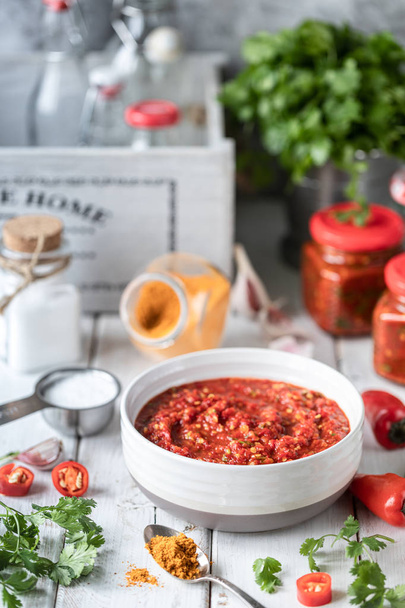 Prozess des Kochens scharfe Soße aus roten Paprika. Zutaten: Pfeffer, Gemüse, Basilikum, Paprika auf einem Holztisch. Glasgefäße mit Fertigsoße. - Foto, Bild
