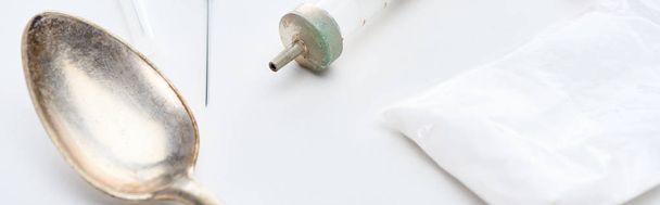 cuchara de plata, jeringa, aguja y heroína sobre fondo blanco, tiro panorámico
 - Foto, Imagen