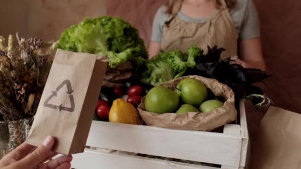 Ανακυκλώσιμη χάρτινη σακούλα στο κατάστημα λαχανικών. Γυναίκα πωλητής βάζοντας φαγητό σε φιλικές προς το οικολογικό χαρτοσακούλες. Οικολογικές αγορές, κατανάλωση, μηδενικά απορρίμματα, χωρίς πλαστική ύλη  - Πλάνα, βίντεο