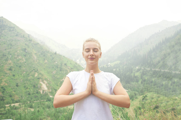 Спортивна дівчина робить йогу в горах красивим пейзажем. Молода заспокоєна жінка веде здоровий спосіб життя, медитує, розслабляє іменну позу в яскравому спортивному одязі на природі
 - Фото, зображення