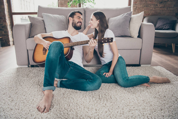 Two nice attractive lovely tender cheerful cheery positive people having fun spending day holiday weekend sitting on floor playing songs melody at home house apartment indoors - Foto, Bild