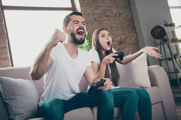 Photo of funny pair sitting sofa indoors playing video games excited by unexpected winning and losing - Foto, imagen
