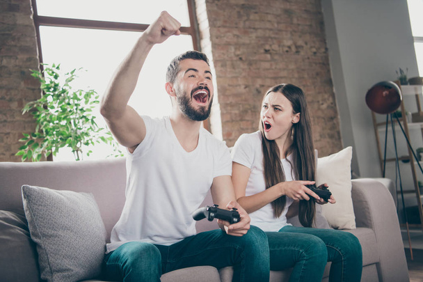 Photo of funny pair sitting sofa indoors playing video games excited by unexpected winning and losing - Фото, зображення