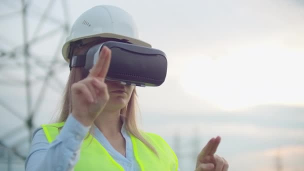 Portret nowoczesnej kobiety z mechaniki inżyniera przeprowadzając inspekcję poprzez okulary wirtualnej rzeczywistości i biały hełm, ubrany w mundur w tle wieże władzy - Materiał filmowy, wideo