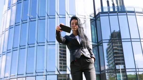 Businesswoman making selfies in front of office building. Smiling lady taking photos for her business partners abroad. Concept of: Lifestyle, Mobile, Selfie, Alone, Summer. - Foto, immagini