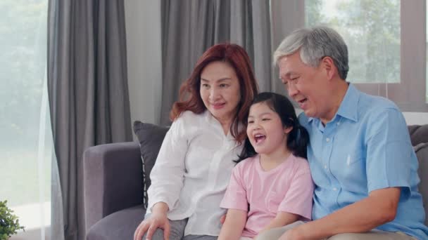 Азіатські бабусі і дідусі дивитися телевізор з внучкою в домашніх умовах. Старший китайський, Дід і бабуся щасливі з використанням сімейного часу розслабитися з молодою дівчиною дитиною, лежачи на дивані в кімнаті вітальні концепцію. Повільний рух. - Кадри, відео
