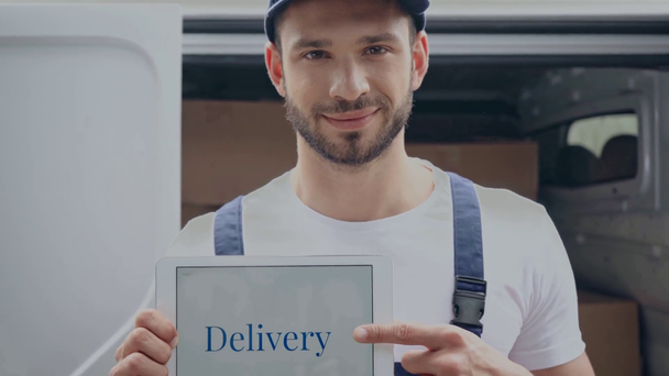 delivery man pointing with finger at digital tablet with delivery word near car - Materiał filmowy, wideo
