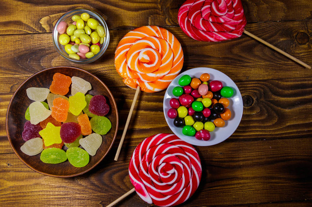 Coloridos caramelos de chocolate, piruletas y dulces de gelatina en la mesa de madera - Foto, Imagen