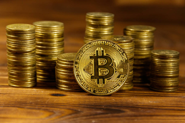 Bitcoin dourado e pilhas de moedas em fundo de madeira
 - Foto, Imagem
