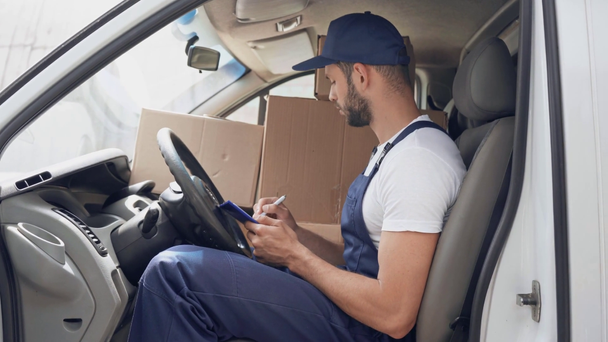 delivery man schrijven op Klembord tijdens het controleren van pakjes in de auto - Video