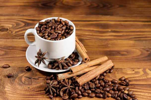 Coffee beans in white cup, cinnamon sticks and star anise on wooden table - Photo, Image