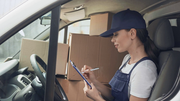 happy delivery woman writing on clipboard in car near parcels - Video