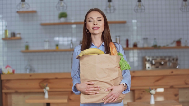 cheerful girl holding paper bag with groceries at home  - Кадри, відео