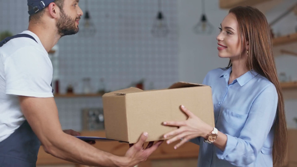 uśmiechnięta kobieta otrzymująca przesyłkę od mężczyzny dostawy w domu - Materiał filmowy, wideo