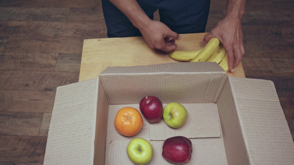 oříznutý pohled na člověka, který dává ovoce do krabice s krabem - Záběry, video