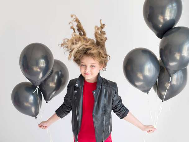 blond model with curly hairstyles in a black leather jacket and with black balloons in their hands on a white background - Photo, Image