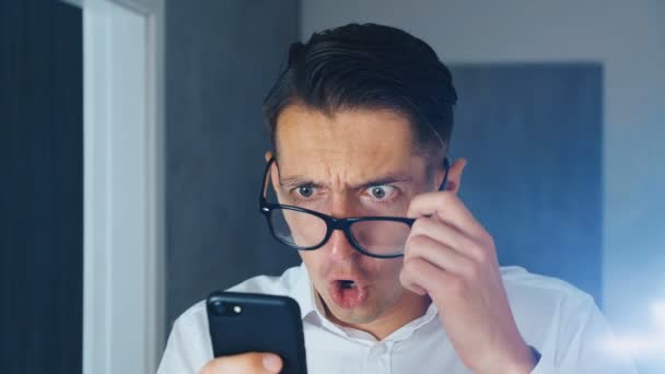 Portrait of shocked and disgusted man. Confused man saw an unpleasant message on a smartphone, in surprise puts off glasses and looks at the camera. He is worried about seeing. Close-up. - Footage, Video