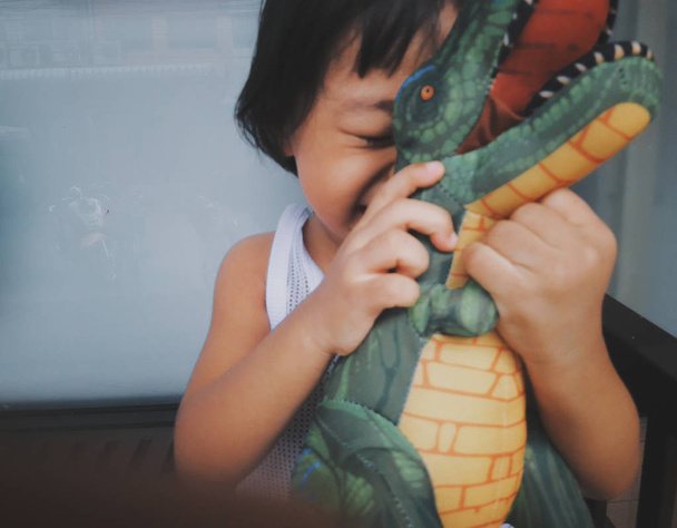 Foto borrosa estilo vintage niño Asia chica abraza dinosaurios muñeca felizmente. Ella se sonríe muy feliz, concepto de niña feliz, Dientes hermosos
. - Foto, imagen
